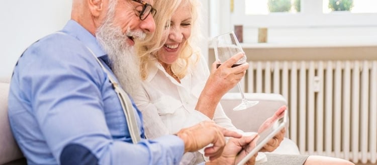 Senior couple, sitting on a sofa, laughing while playing on a computer tablet 