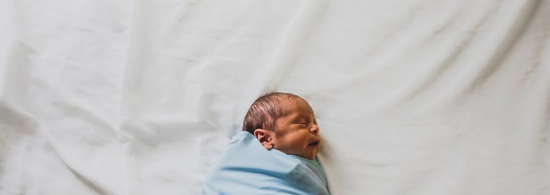 Image of a newborn baby wrapped in a blue blanket lying on a white sheet