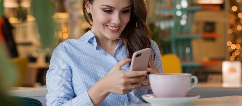 Image shows lady in a cafe, smiling and reading on her smartphone