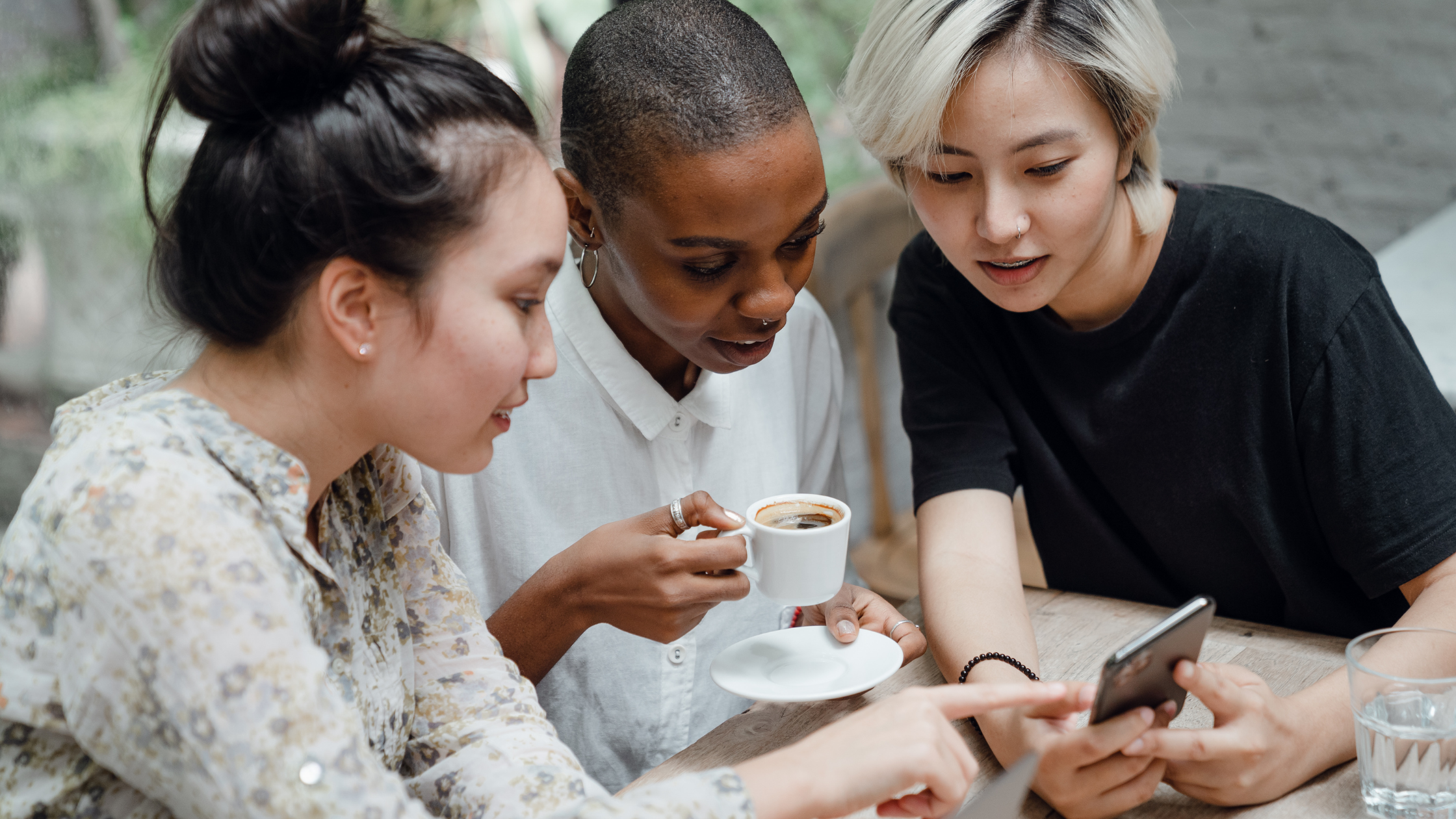 Group of friends sitting together in a cafe, one is showing the others something on her smartphone screen