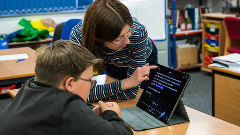 Student and TA review text on a tablet in a classroom. The tablet displays a book on EasyReader App with accessibility features