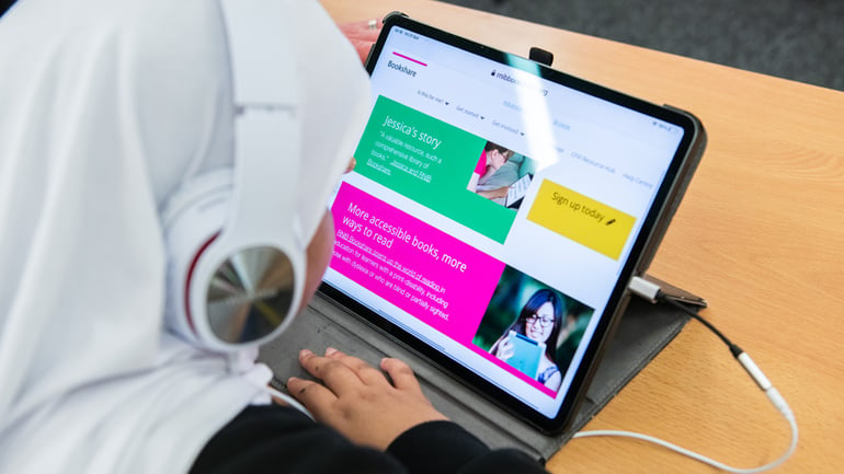 Young girl wearing headphones visits the RNIB Bookshare website on a Windows tablet.