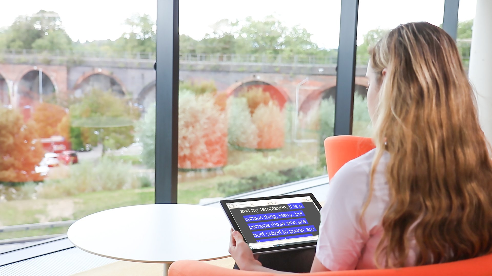 Teenage girl sitting at a table reading a book on a tablet 