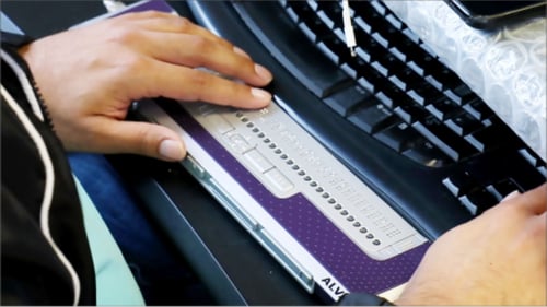 Image shows Aj's hands using a Braille display and computer keyboard