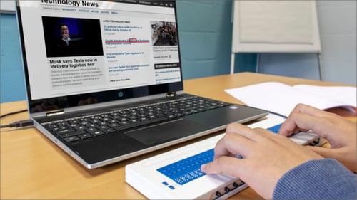 Image shows a laptop displaying SuperNova Screen Reader and a person using a Braille keyboard to read whats on screen