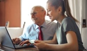 Image shows younger lady and older man working on a laptop together-1
