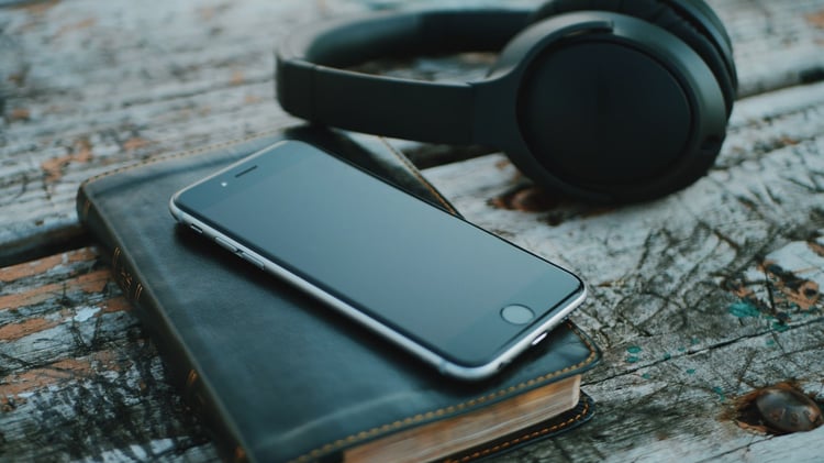 Image shows a book, smartphone and headphones on a wooden table