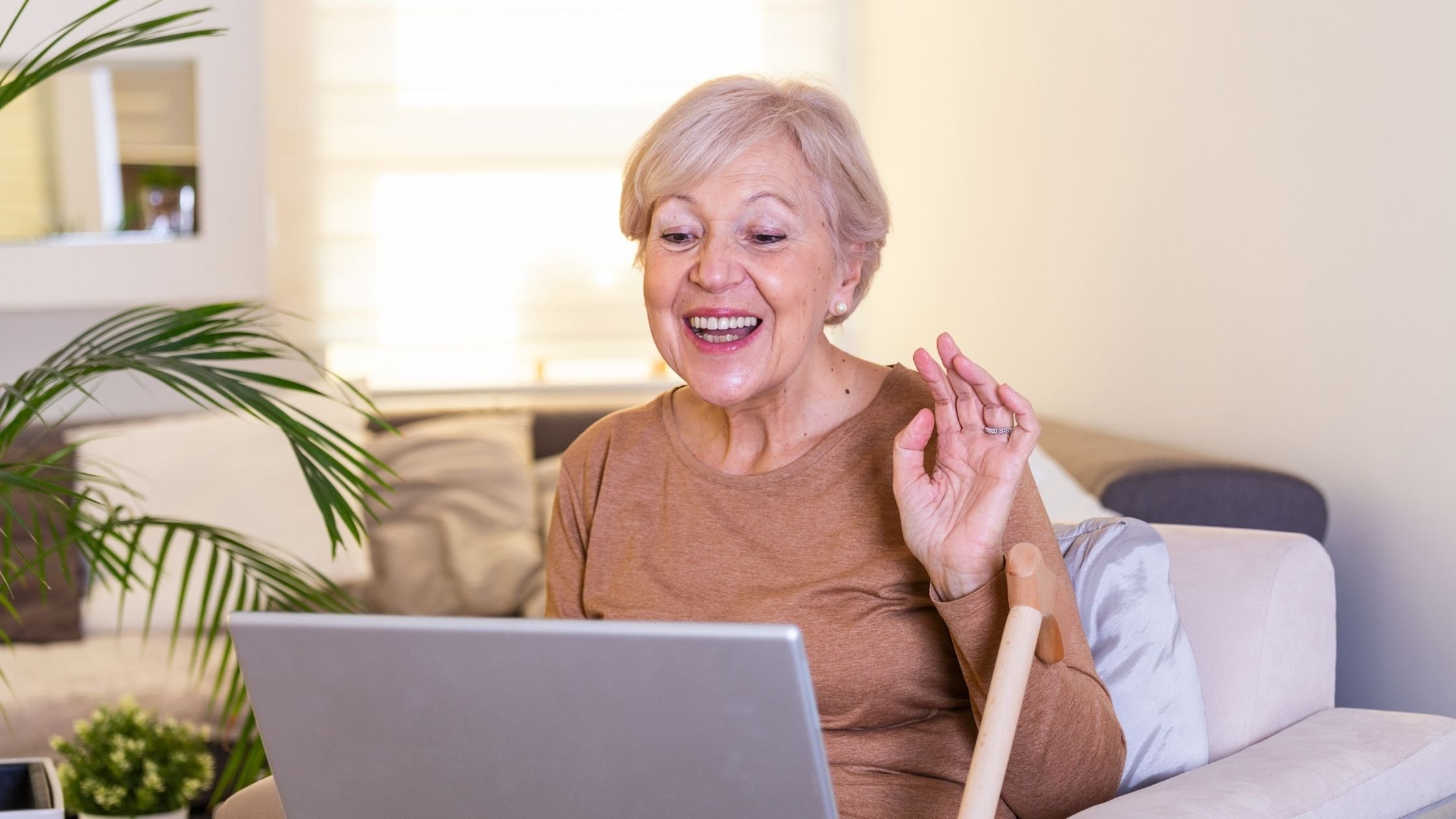 Lady on sofa waves happily towards laptop computer screen