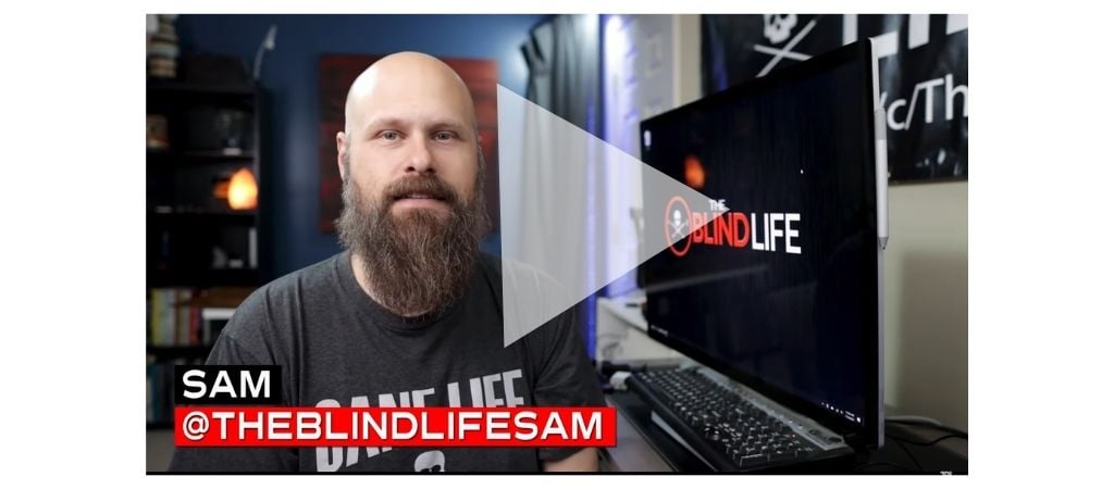 Sam from The Blind Life sitting at his computer desk - a large play button is overlaid