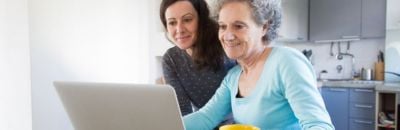 Mother and grown-up daughter looking at a laptop in a sunny kitchen