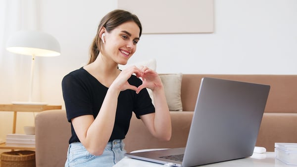 Young lady makes heart shape with her hands while on video call