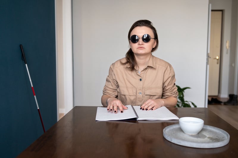 Woman reading a braille embossed document in an interview room. Her cane leans against the wall next to her.