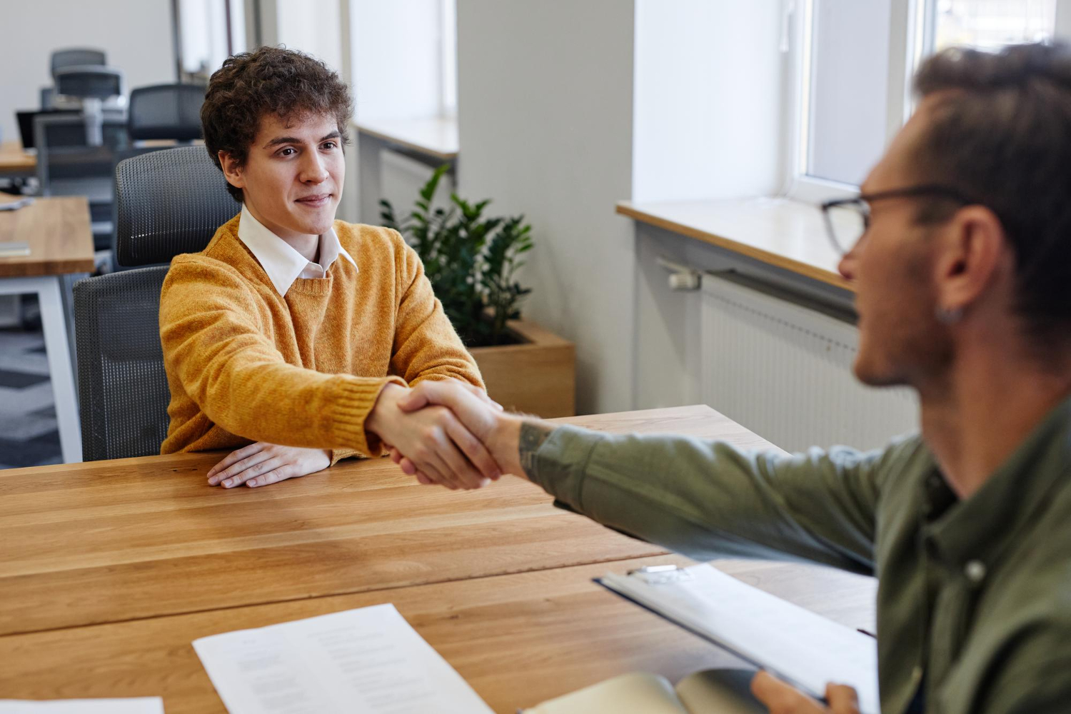 Young man in a yellow sweater shaking the hand of his new employer after accepting a job offer