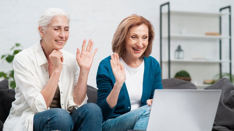 two friends wave and smile toward open laptop on video call